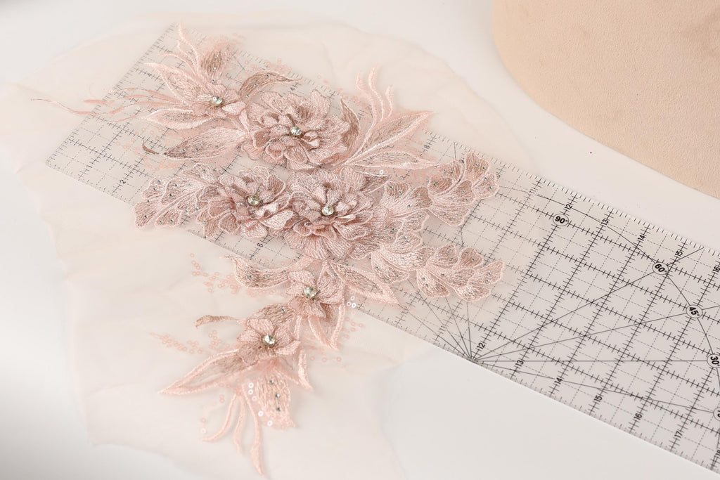 a delicate floral embroidery with pink flowers and leaves, placed on a transparent ruler.