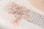 a delicate floral embroidery with pink flowers and leaves, placed on a transparent ruler.