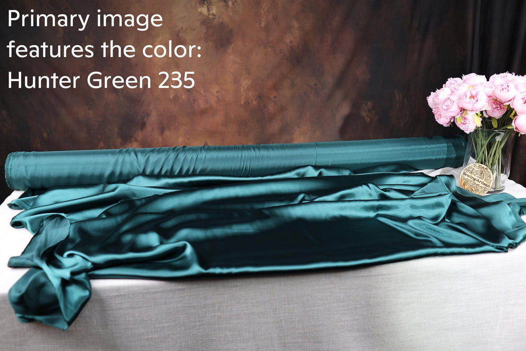 a roll of green satin fabric with the text "Hunter Green 235" on it, placed on a table next to a vase of pink flowers.