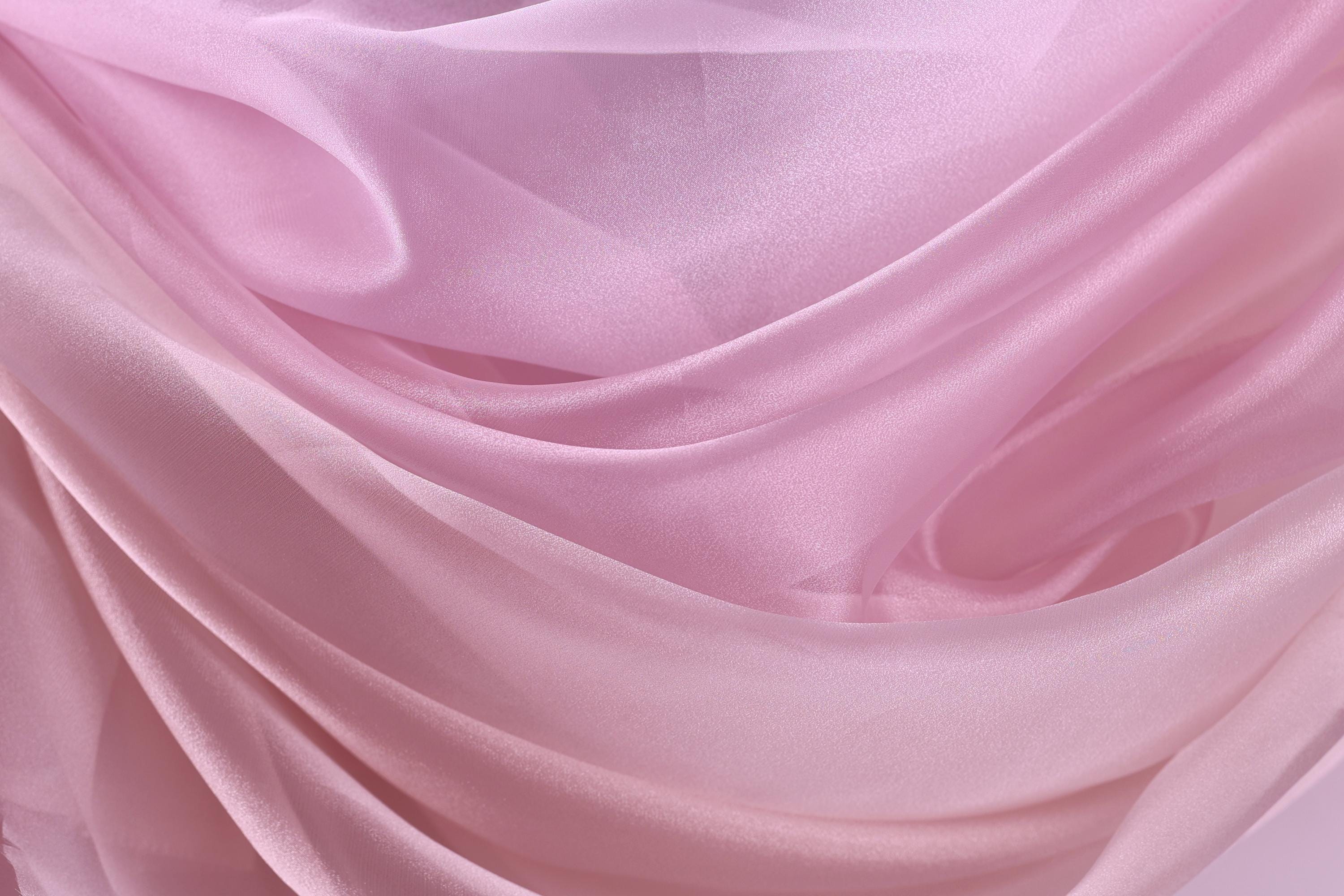 The image is a close-up of a soft, flowing fabric in shades of pink and white, creating a visually appealing and delicate texture.