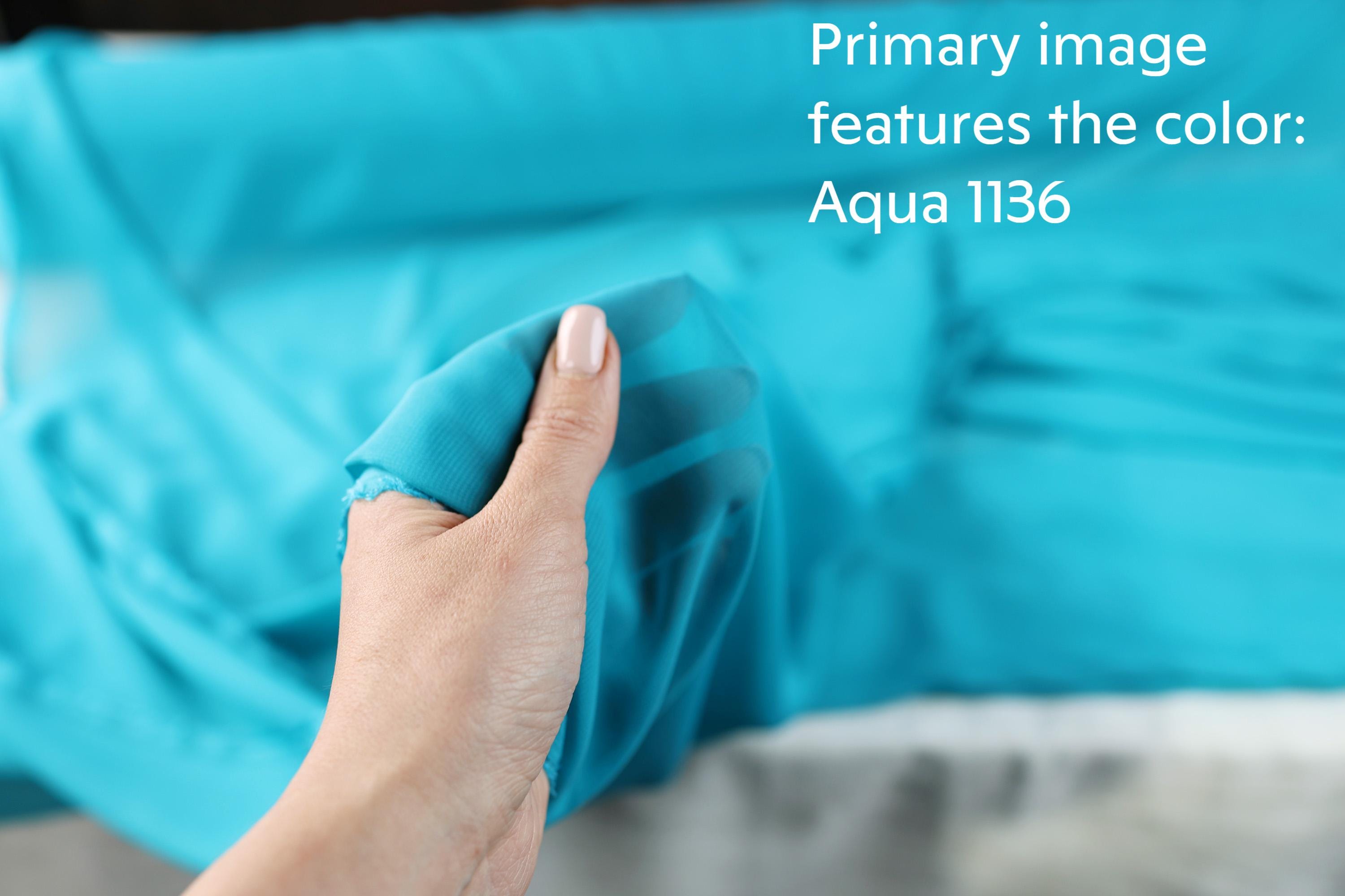 A hand holding a piece of blue fabric, with a blurred background of the same blue fabric.