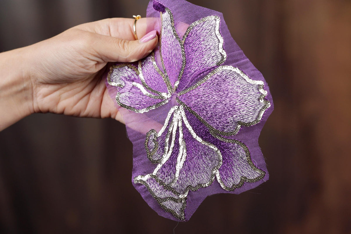A hand holding a purple flower embroidered on a piece of fabric.