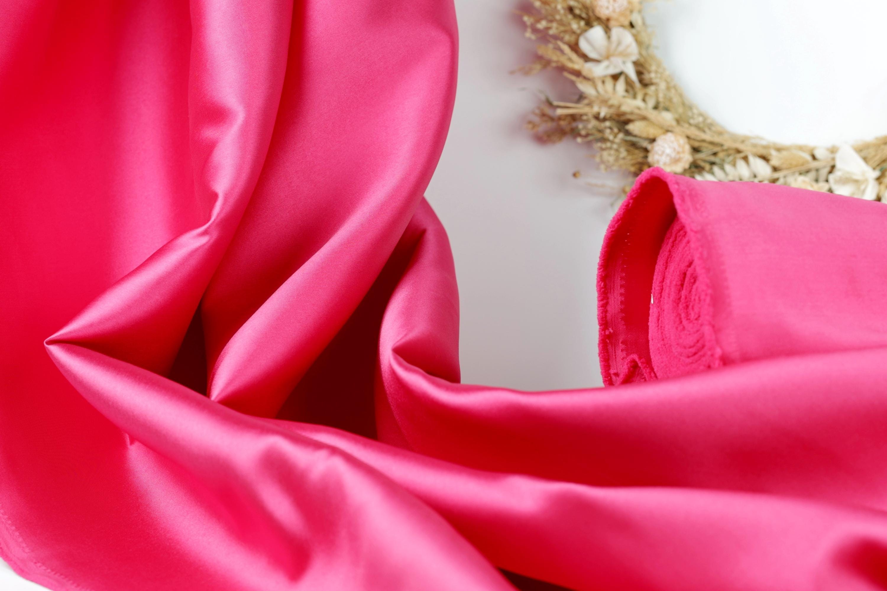 A close-up view of a vibrant pink satin fabric, with a wreath made of dried flowers and greenery placed next to it.