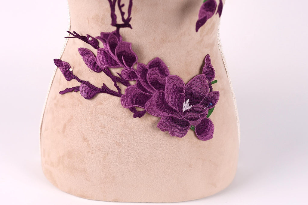 a close-up view of a beige fabric with a purple flower embroidered on it.