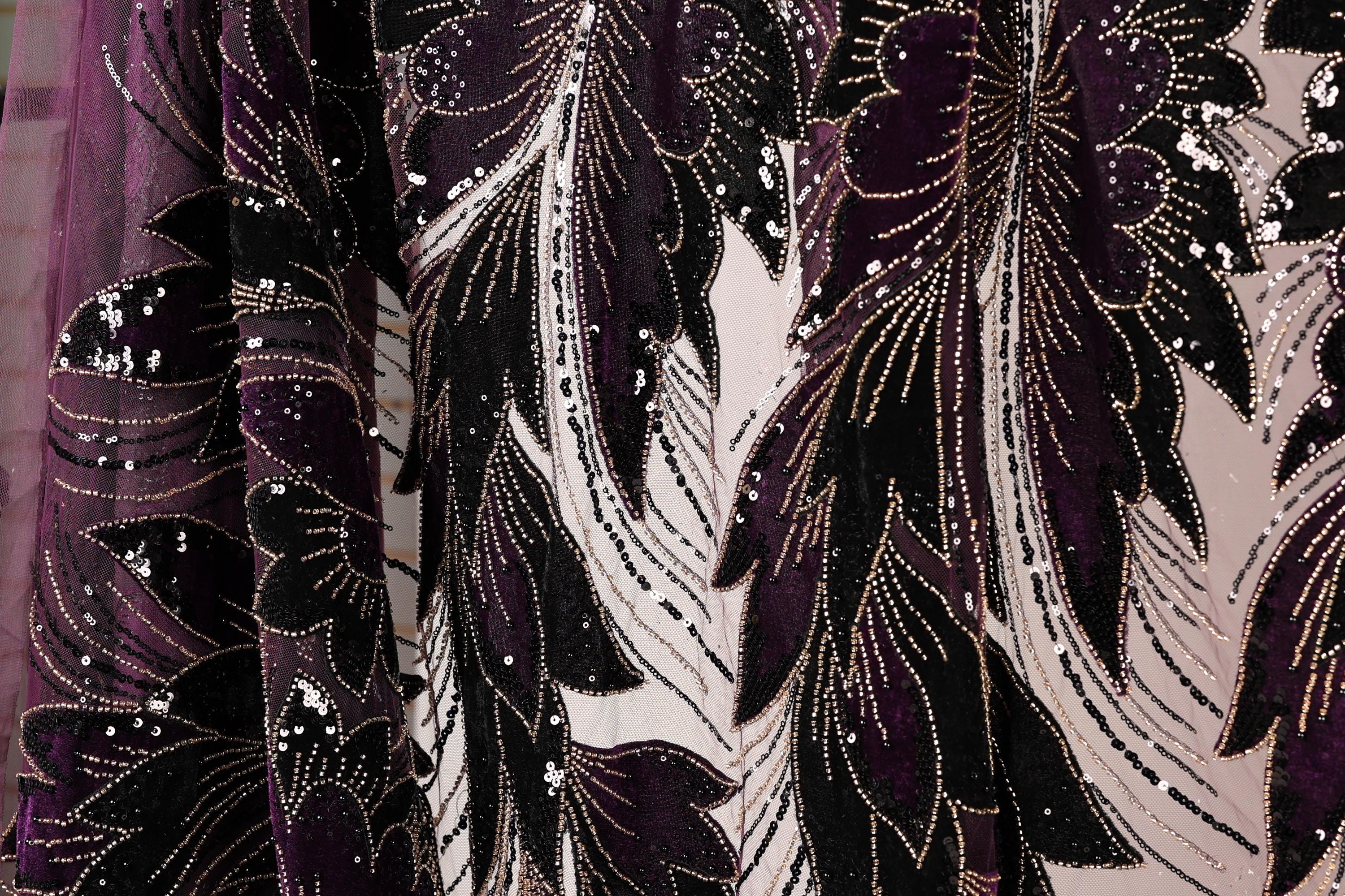 a close-up view of a fabric with a floral pattern in shades of purple and black, adorned with sequins.