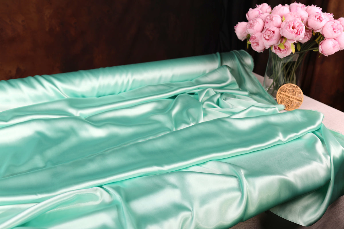 a turquoise satin fabric draped over a table, with a vase of pink roses placed next to it.