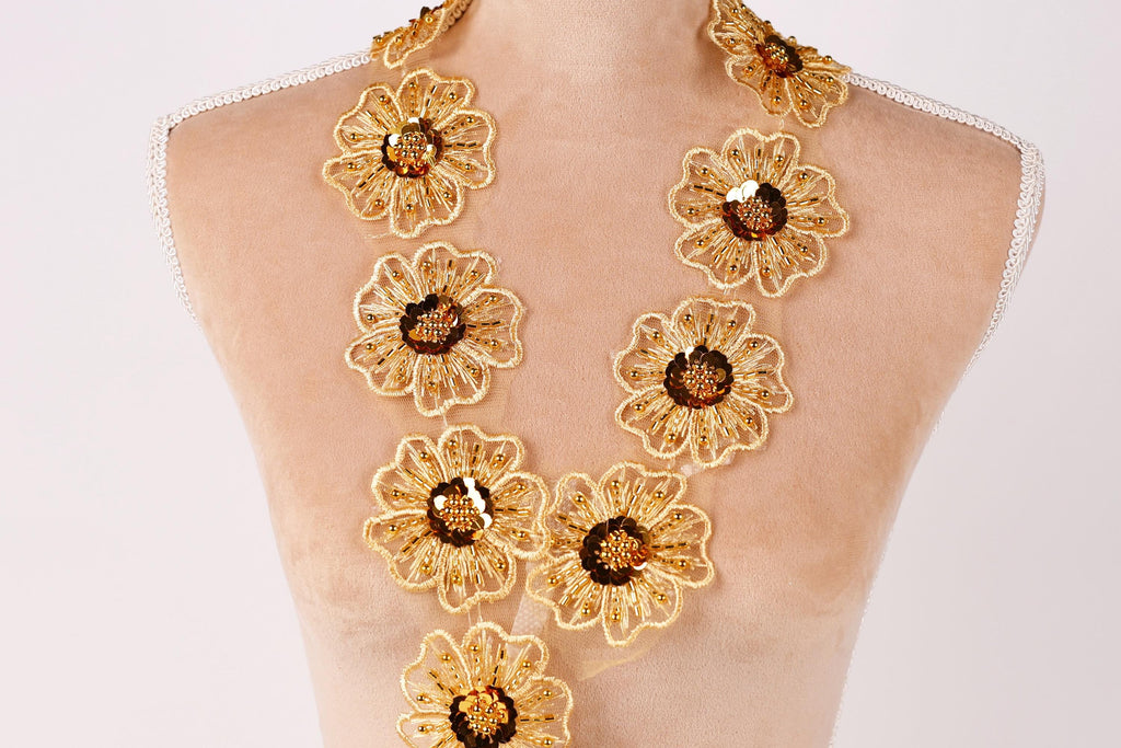 A mannequin wearing a gold necklace with large, intricately designed flower-shaped pendants.