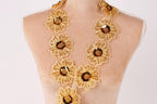 A mannequin wearing a gold necklace with large, intricately designed flower-shaped pendants.