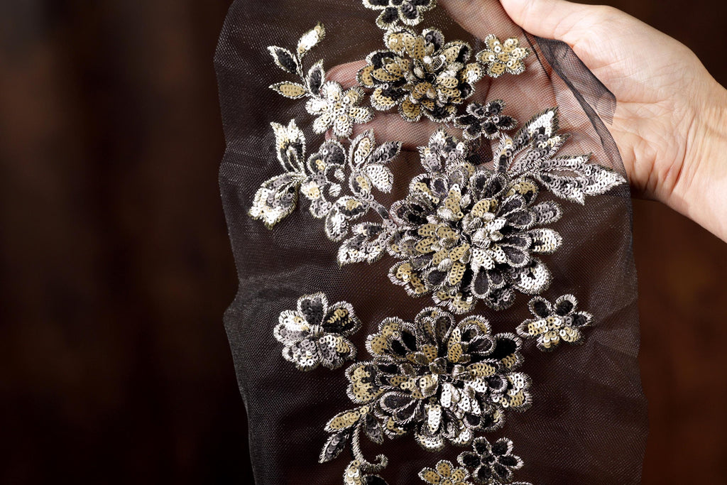 A hand is holding a piece of fabric with intricate floral embroidery on it.