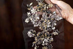 A hand is holding a piece of fabric with intricate floral embroidery on it.