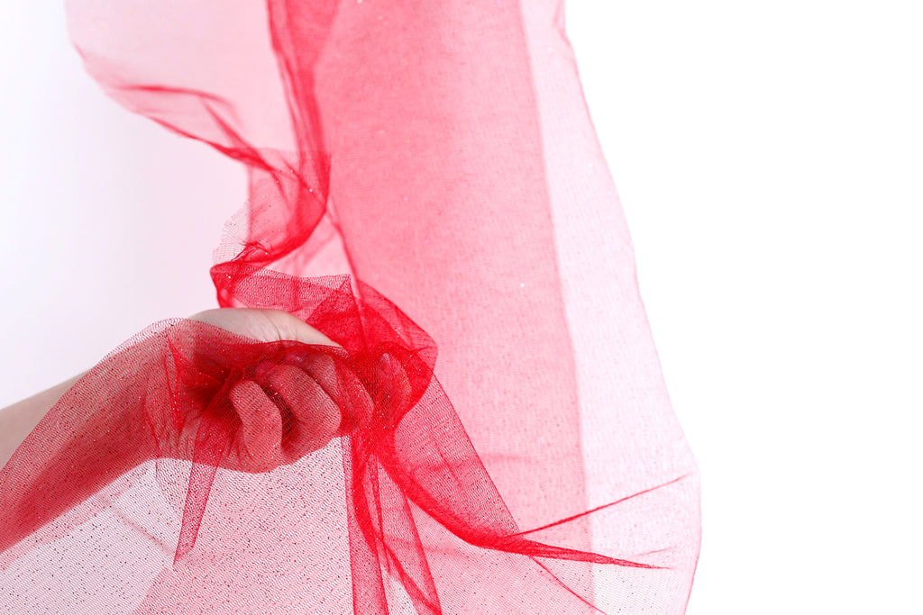 A hand is holding a red, sheer fabric or tulle material, with the fabric being slightly crumpled.