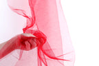 A hand is holding a red, sheer fabric or tulle material, with the fabric being slightly crumpled.