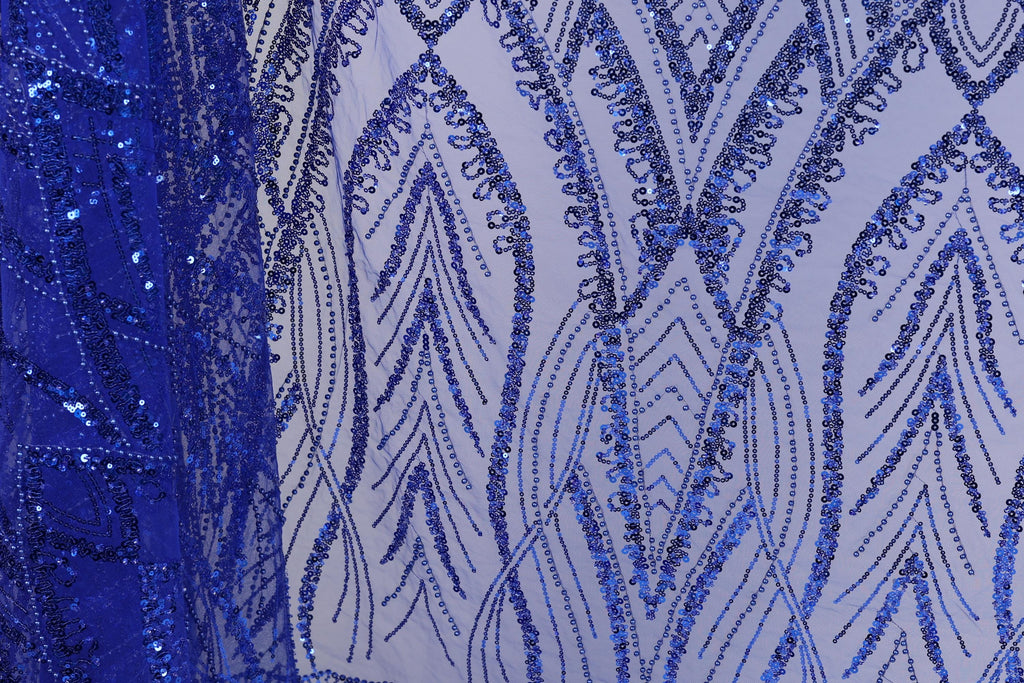 a close-up view of a fabric with a striking blue sequin pattern. The pattern is intricate and detailed, with a repeating design of blue sequins arranged in a zigzag pattern across the fabric. The fabric appears to be a sheer material, allowing the blue sequins to stand out prominently. The image does not contain any text or other discernible objects, and the focus is solely on the detailed blue sequin pattern.