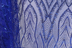 a close-up view of a fabric with a striking blue sequin pattern. The pattern is intricate and detailed, with a repeating design of blue sequins arranged in a zigzag pattern across the fabric. The fabric appears to be a sheer material, allowing the blue sequins to stand out prominently. The image does not contain any text or other discernible objects, and the focus is solely on the detailed blue sequin pattern.