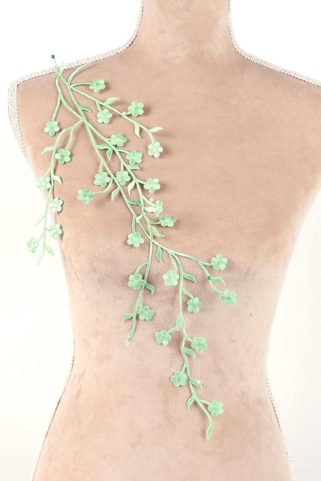 A mannequin torso with a green floral branch or branch-like object attached to it.