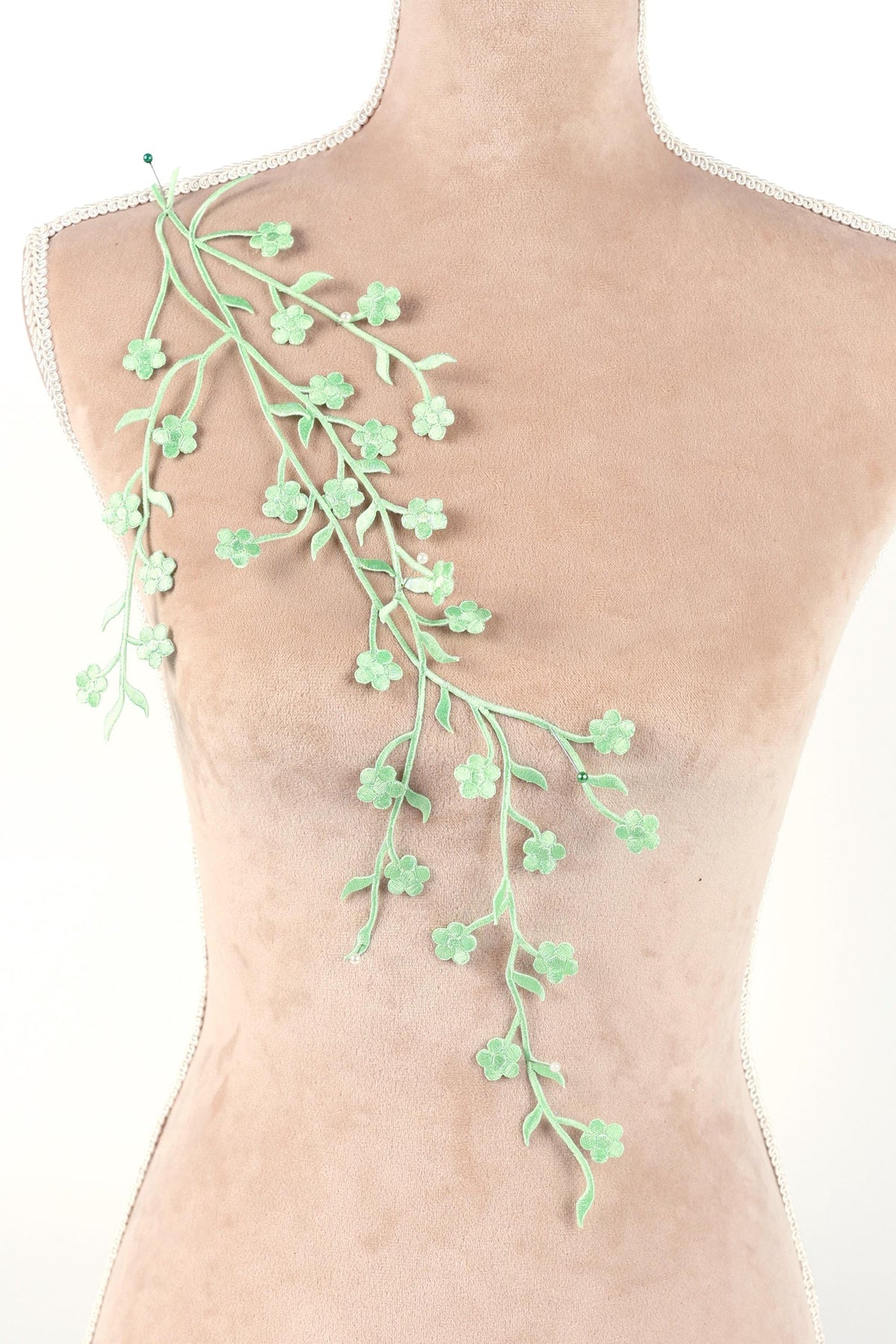 A mannequin torso with a green floral branch or branch-like object attached to it.