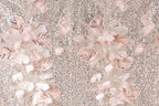 a close-up view of a fabric with a floral pattern, including pink and white flowers and leaves. The fabric appears to be made of sequin material, giving it a shiny and textured appearance.