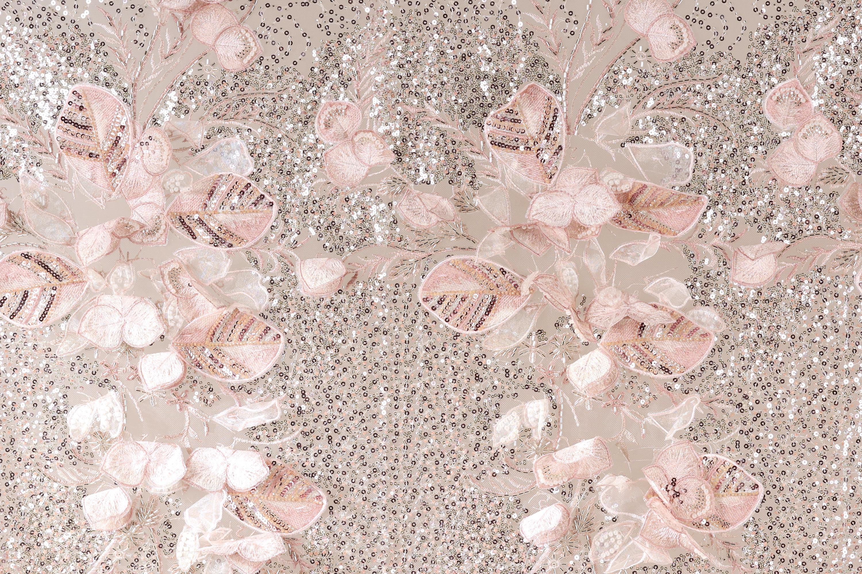 a close-up view of a fabric with a floral pattern, including pink and white flowers and leaves. The fabric appears to be made of sequin material, giving it a shiny and textured appearance.