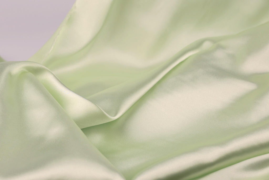 A close-up view of a soft, flowing green satin fabric, with its smooth and shiny texture visible.