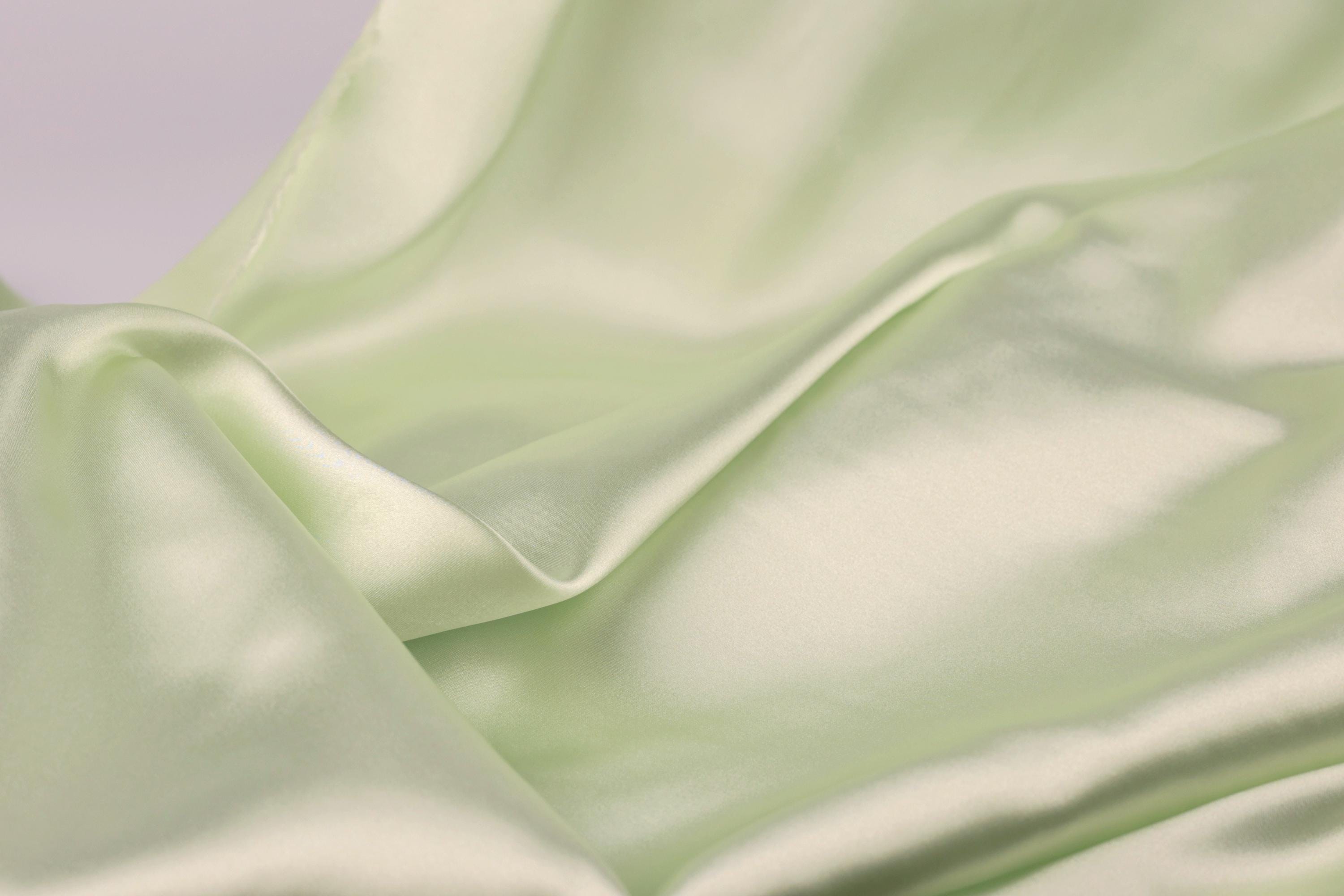 A close-up view of a soft, flowing green satin fabric, with its smooth and shiny texture visible.