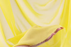 A hand is holding a yellow fabric against a yellow background.