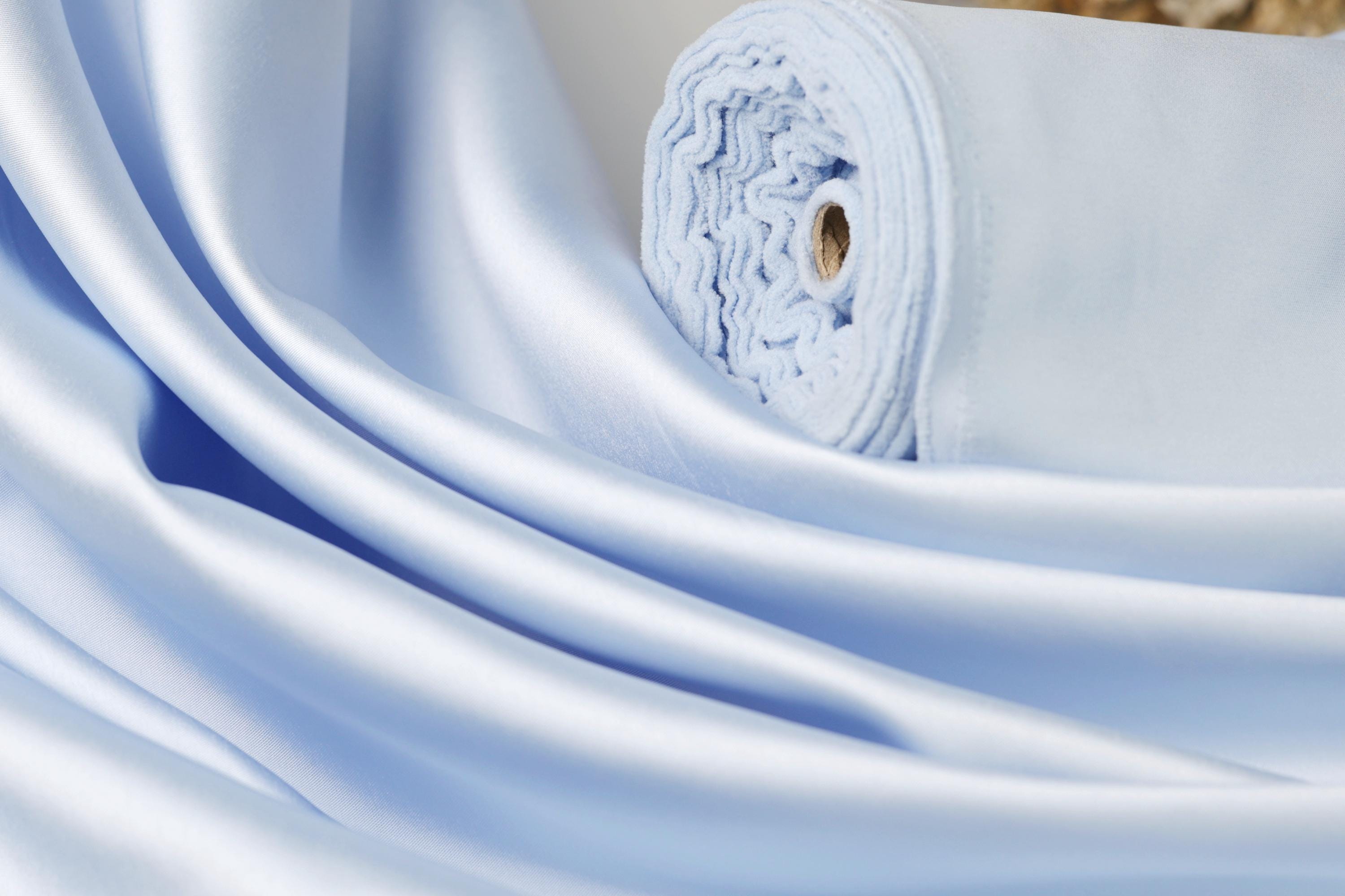 A close-up view of a light blue satin fabric, with its folds and creases visible.