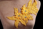 A close-up of a mannequin torso with a decorative gold embroidered flower on the left side.