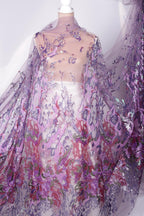 a mannequin wearing a sheer, flowy dress with a floral pattern in shades of purple and pink. The dress appears to be made of a sheer fabric, giving it a delicate and airy appearance.