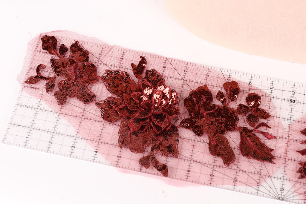 a close-up view of a red sequin flower on a transparent ruler, with the ruler's grid lines visible.