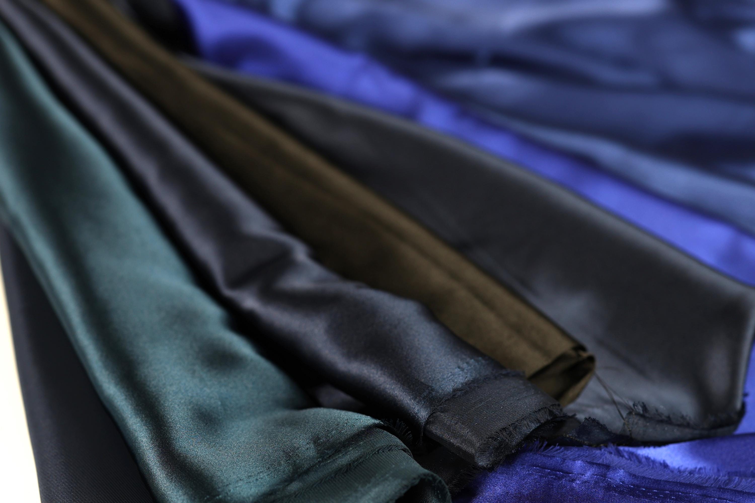 A close-up view of various colored satin fabric, including shades of blue, green, and brown, arranged in a pile.