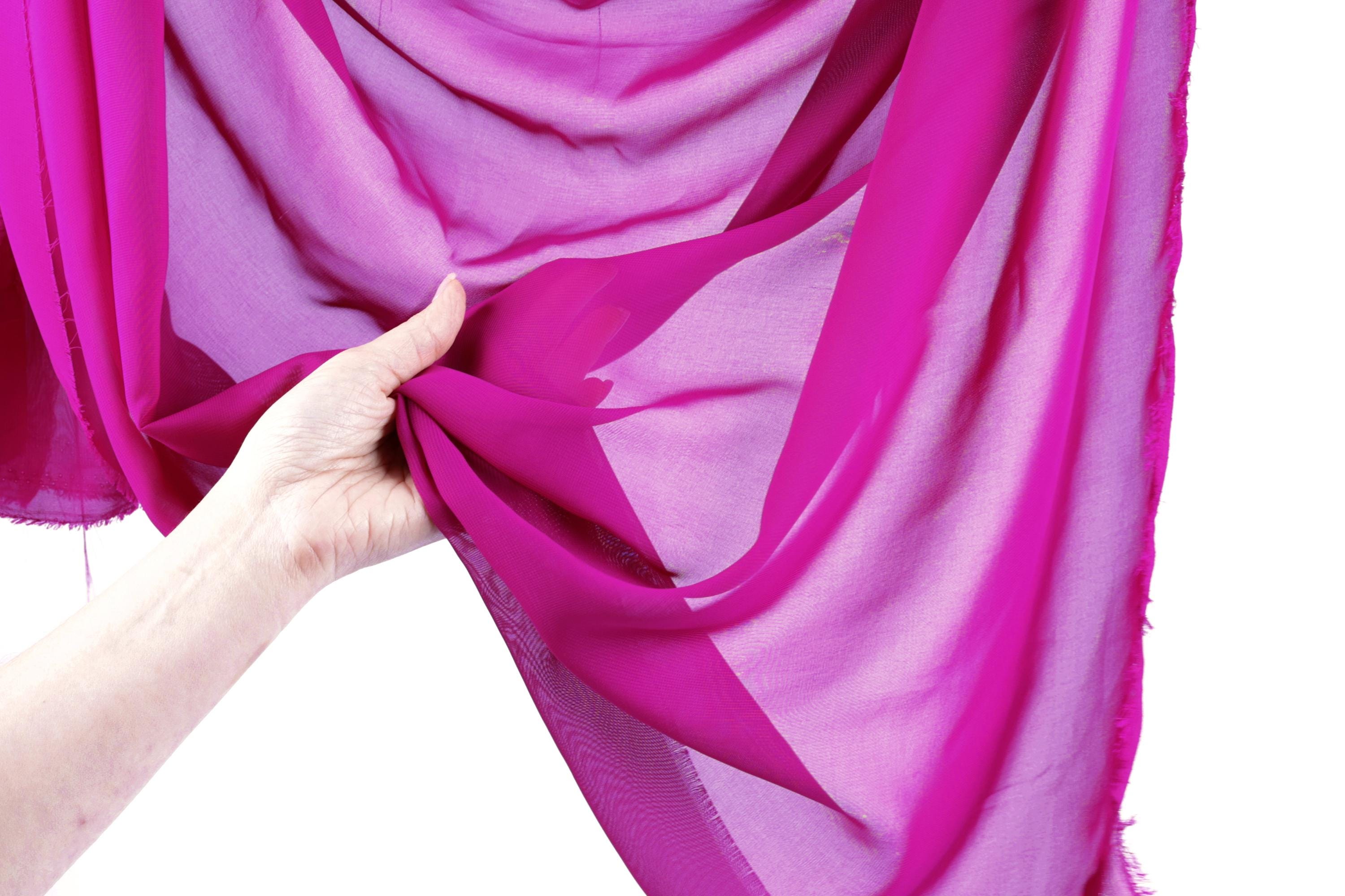 A hand is holding a piece of pink fabric, which appears to be a sheer or sheer-like material.