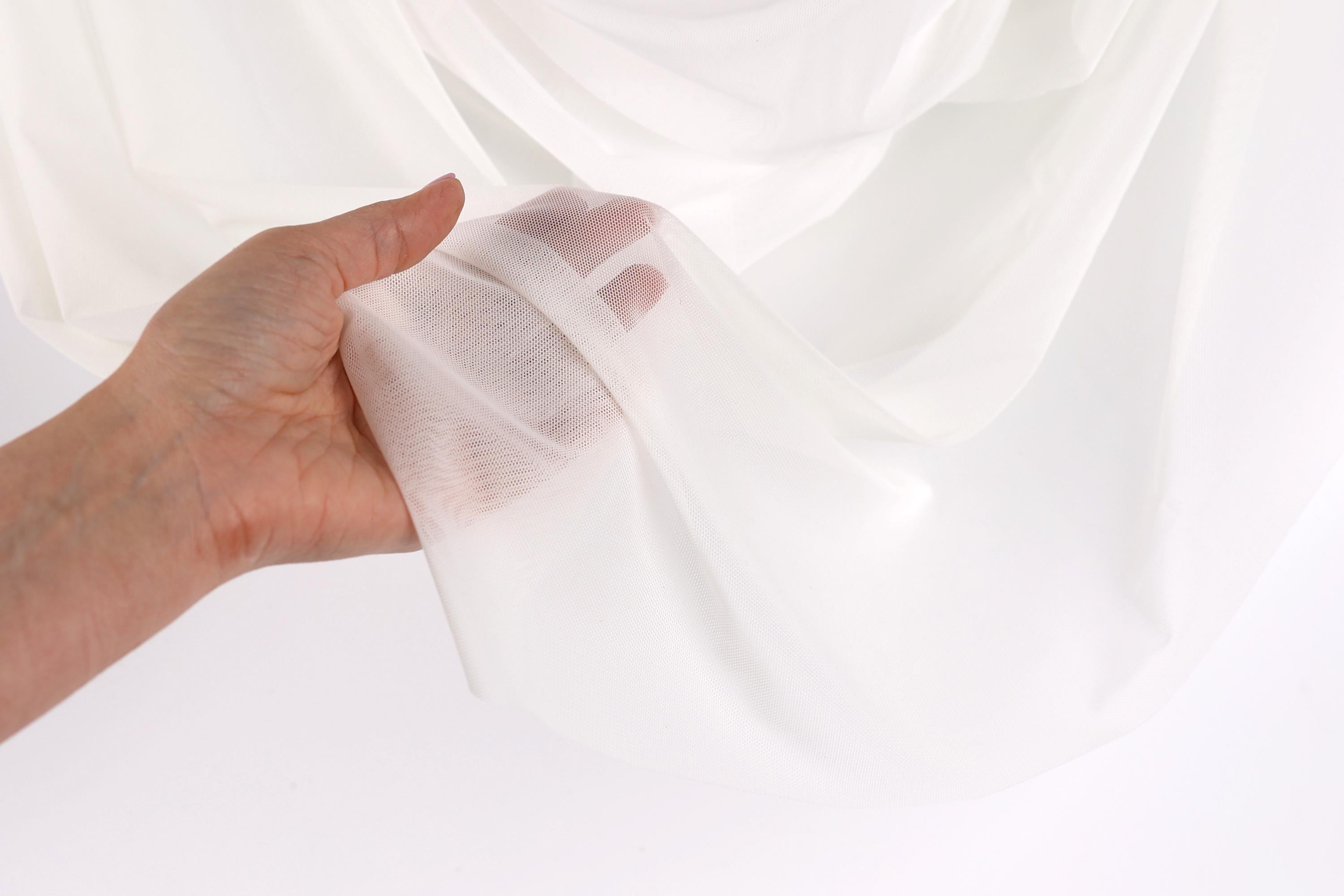 A hand is holding a white fabric, possibly a sheer or sheer-like material, against a white background.