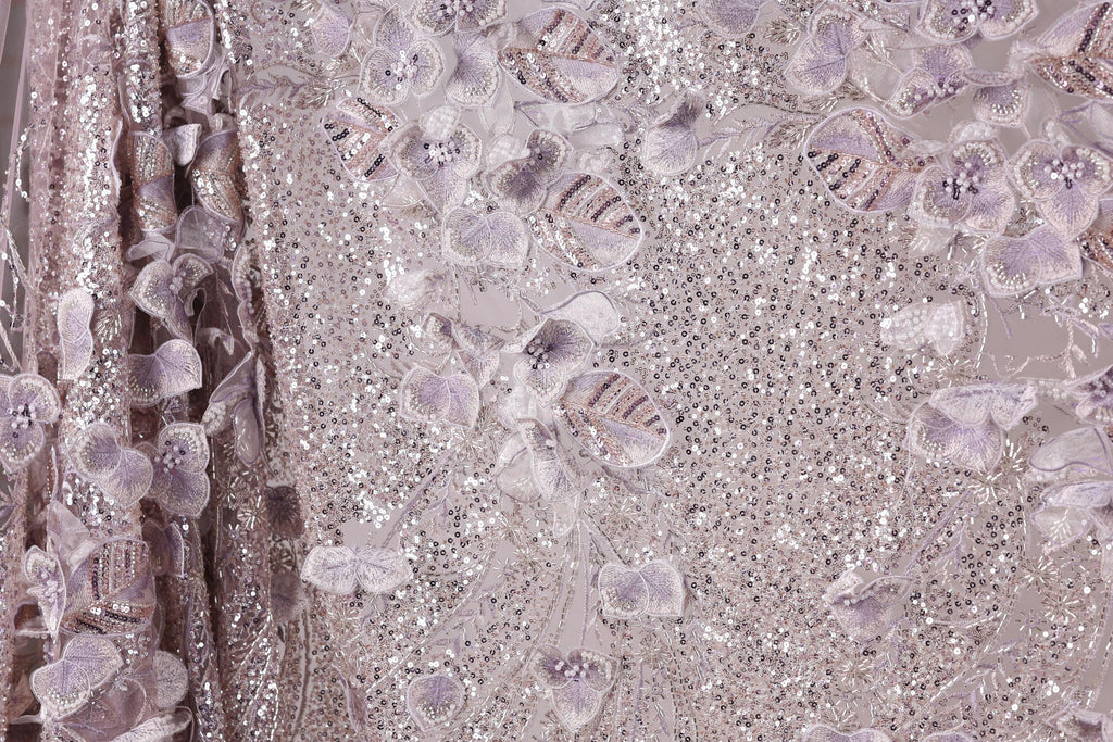 The image is a close-up of a fabric with a floral pattern, featuring a variety of purple and white flowers and sequins.