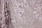 The image is a close-up of a fabric with a floral pattern, featuring a variety of purple and white flowers and sequins.