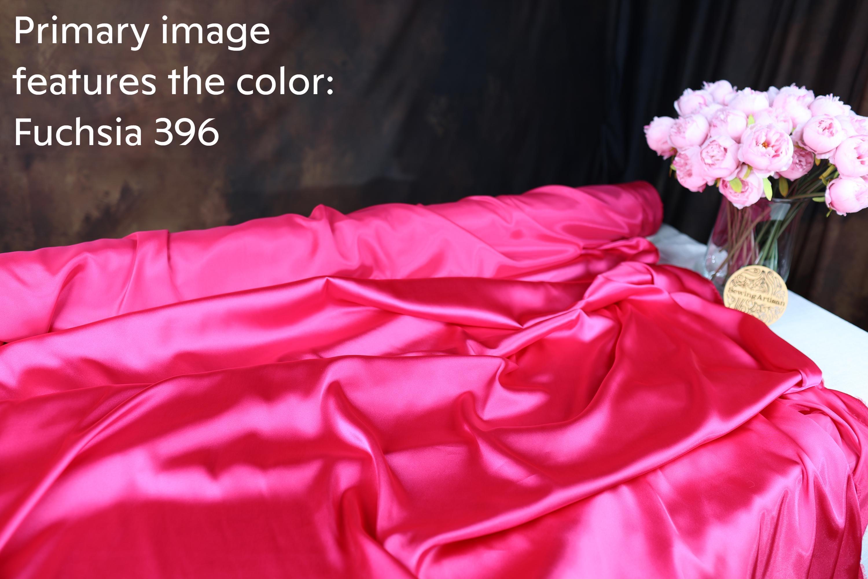 a vibrant pink satin fabric, with a vase of pink flowers placed next to it. The background is dark, creating a contrast that highlights the colors of the fabric and flowers.