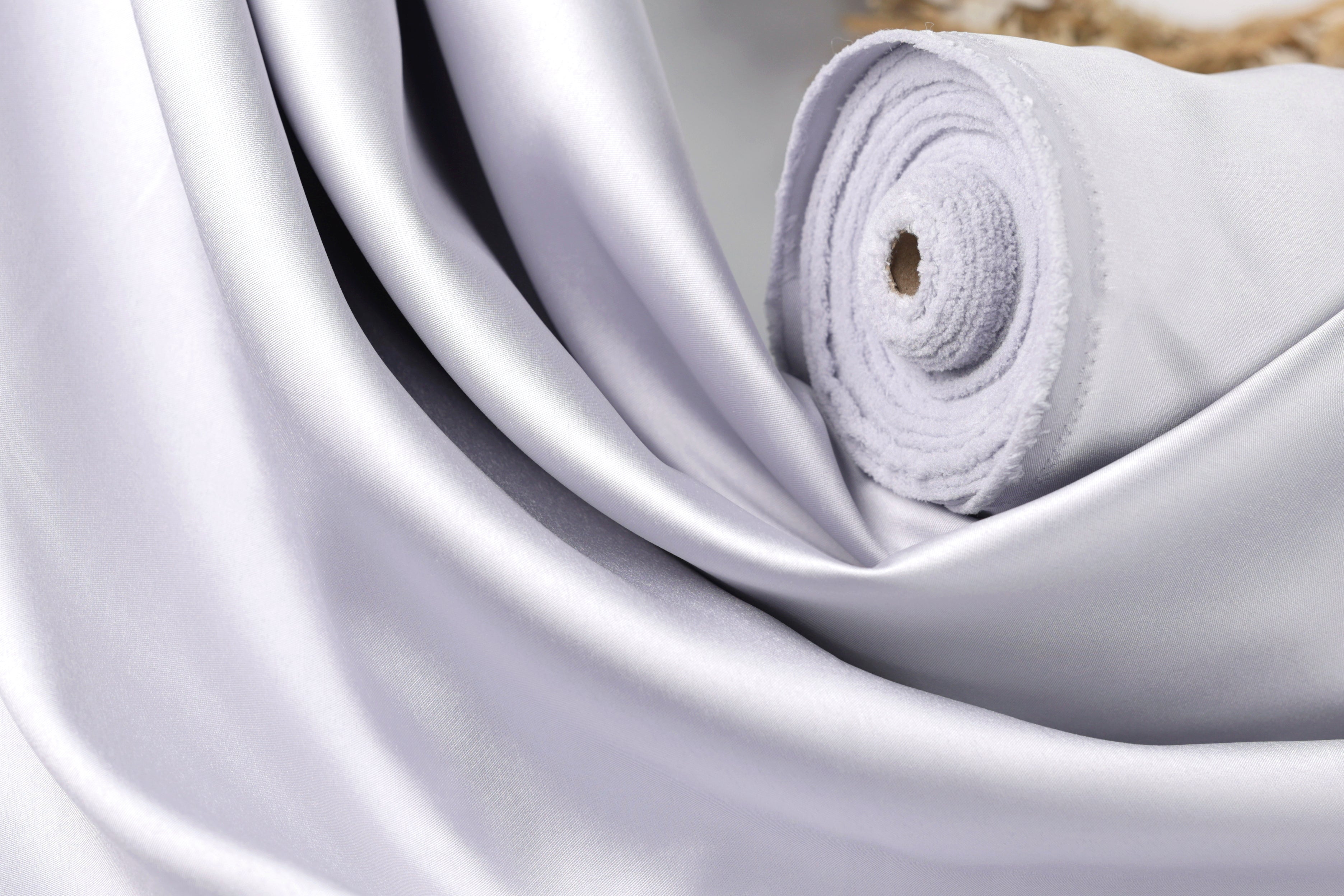 A close-up view of a white satin fabric, possibly silk, with a smooth and shiny texture.