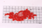 a red lace-like fabric placed on a ruler, which is used for measuring or cutting the fabric.