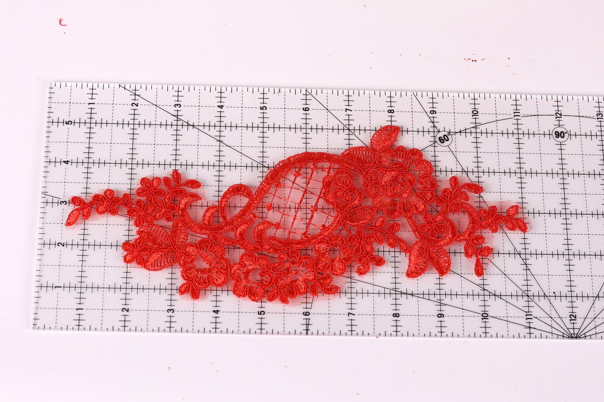 a red lace-like fabric placed on a ruler, which is used for measuring or cutting the fabric.