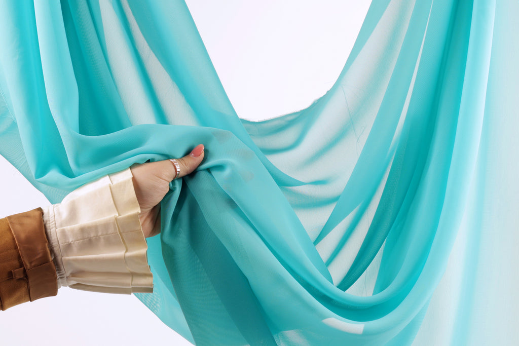 A hand is holding a piece of blue fabric, which appears to be a sheer or sheer curtain.