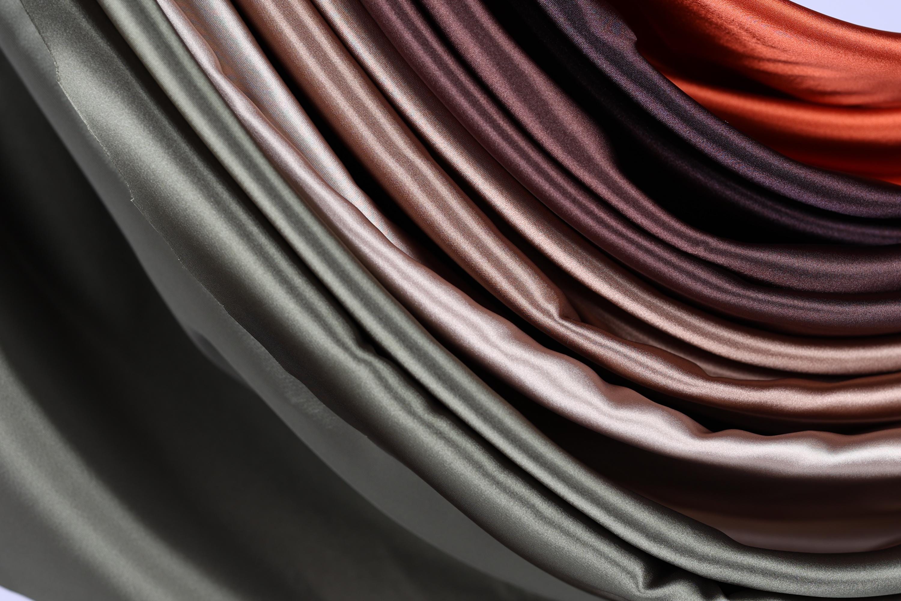 A close-up view of a collection of colorful satin fabric, with a gradient of colors ranging from dark to light brown.