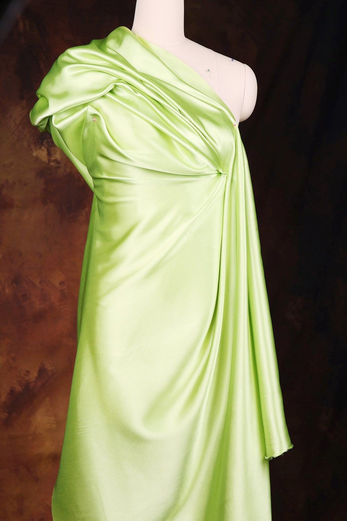A mannequin wearing a bright green one-shoulder dress with a draped, flowing silhouette.