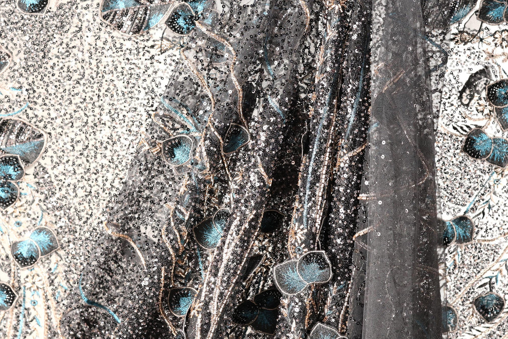 The image is a close-up of a fabric with a black and white pattern, featuring a mix of blue and black elements. The fabric appears to be made of sequin material, with a floral pattern visible on the left side.