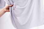 A hand is holding a piece of white fabric, which appears to be a sheer or sheer-like material.