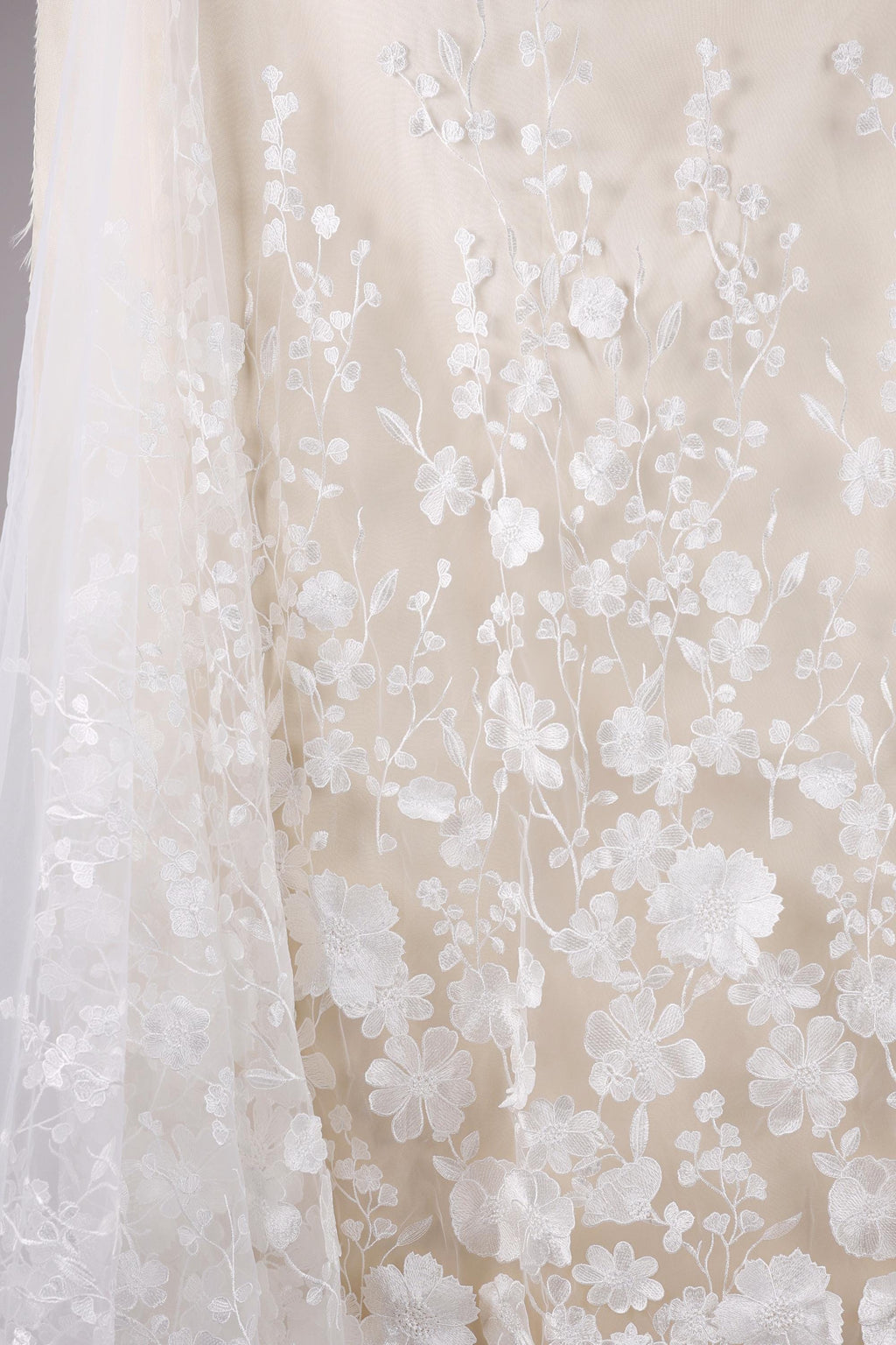 a close-up view of a delicate, white lace fabric with intricate floral embroidery. The fabric appears to be a wedding dress or a similar elegant garment, with the lace and floral patterns creating a visually appealing and delicate design.