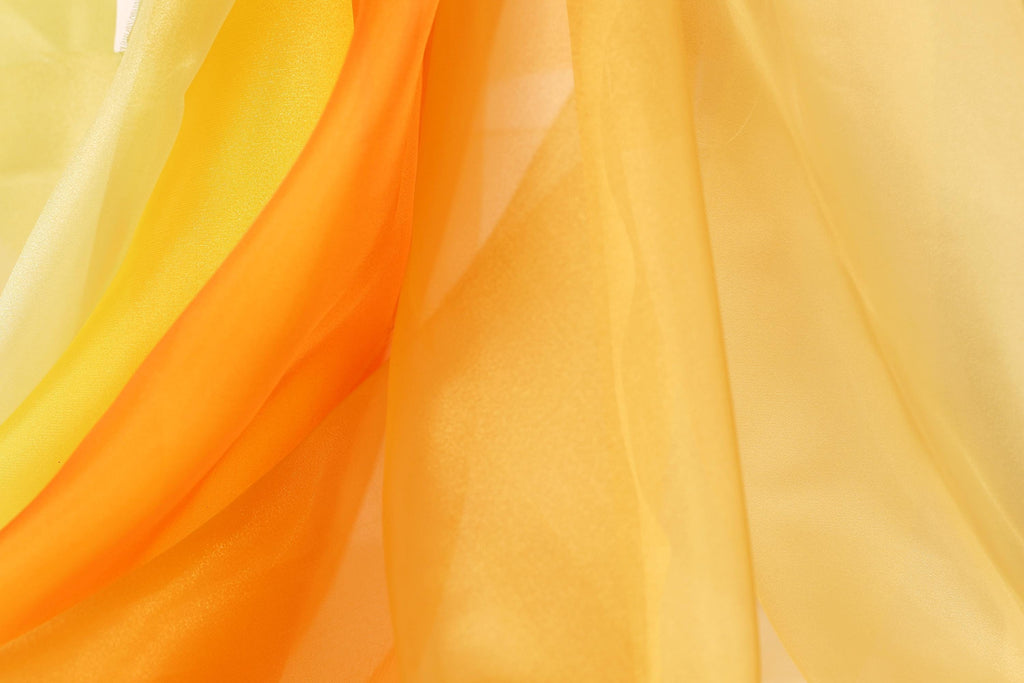 The image is a close-up of a fabric with a yellow and orange color scheme, featuring a soft, flowing texture.