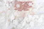 A hand is holding a delicate white lace fabric adorned with white flowers, creating a beautiful and intricate design.