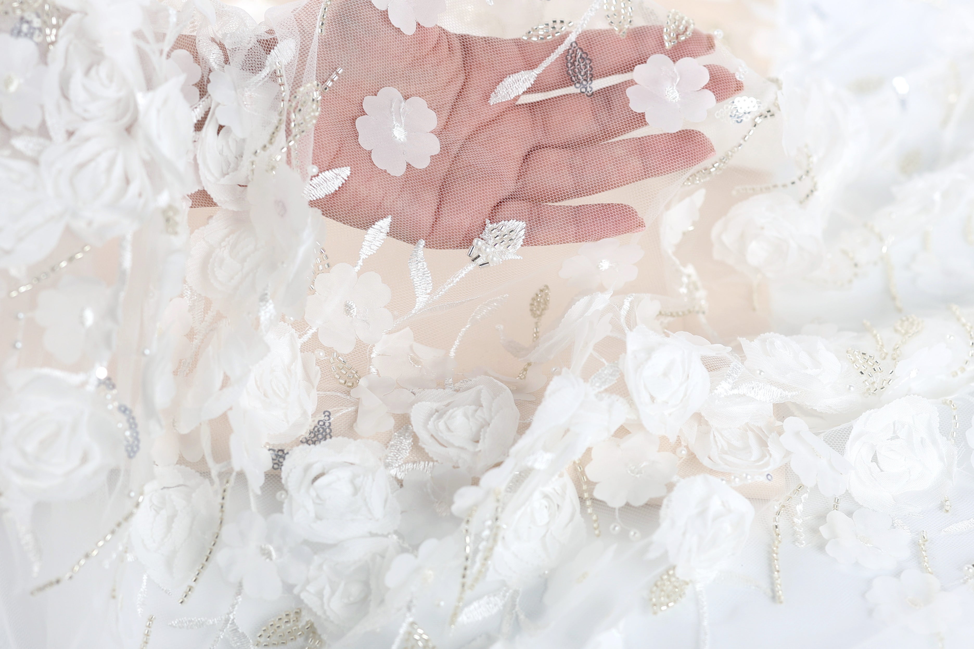 A hand is holding a delicate white lace fabric adorned with white flowers, creating a beautiful and intricate design.