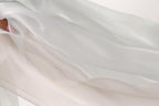 The image is a close-up of a flowing, light-colored fabric, possibly silk or chiffon, with a soft, delicate texture.