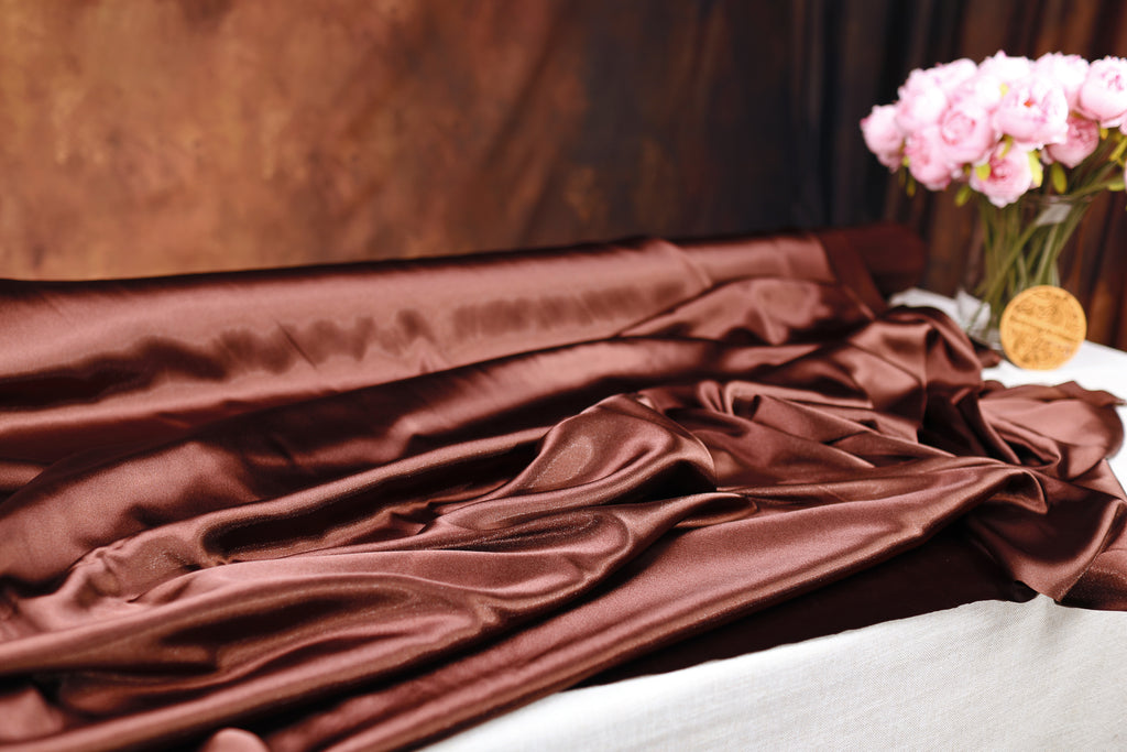 a close-up of a brown satin fabric with a vase of pink flowers on a table.