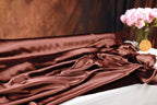 a close-up of a brown satin fabric with a vase of pink flowers on a table.